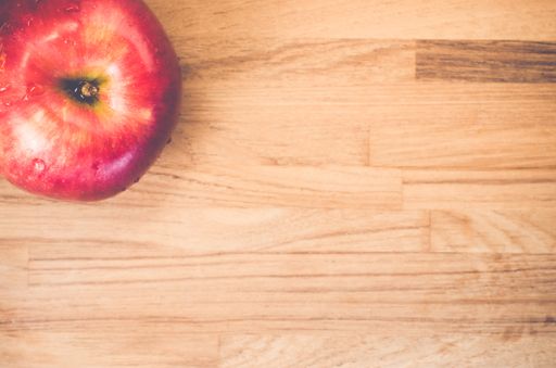 A top view closeup of a big juicy red apple with water drops on it placed on a wooden table