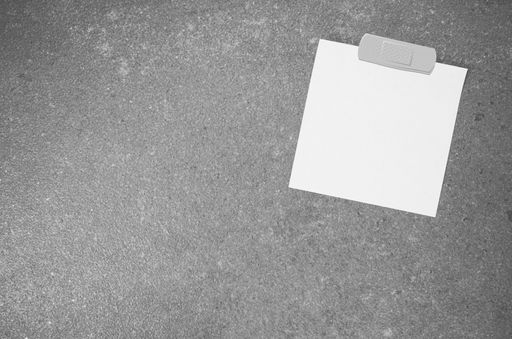 A top view closeup of a white memo paper on a toned rough stone textured surface