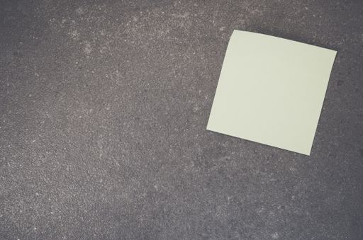 A top view closeup of a white memo paper on a toned rough stone textured surface