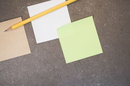 A top view closeup of colorful memo papers and a pencil on a toned rough stone textured surface