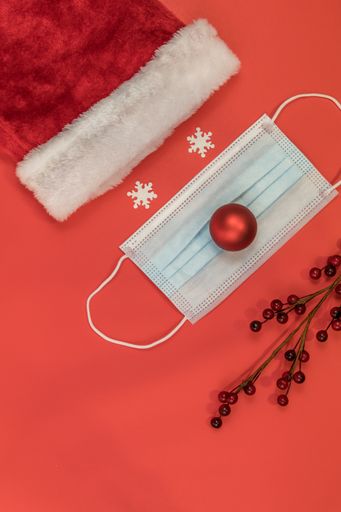 A vertical shot of a Santa Clause hat and a surgical mask on a red surface