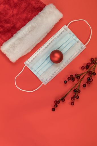 A vertical shot of a Santa Clause hat and a surgical mask on a red surface