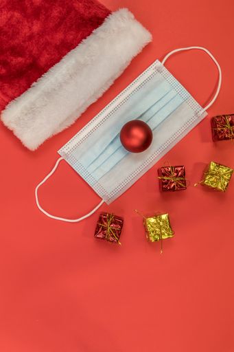 A vertical shot of a Santa Clause hat and a surgical mask on a red surface