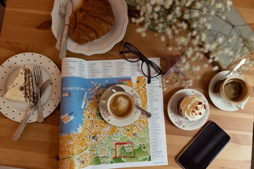 A top view of desserts and cups of coffee on a wooden table with a newspaper and a book