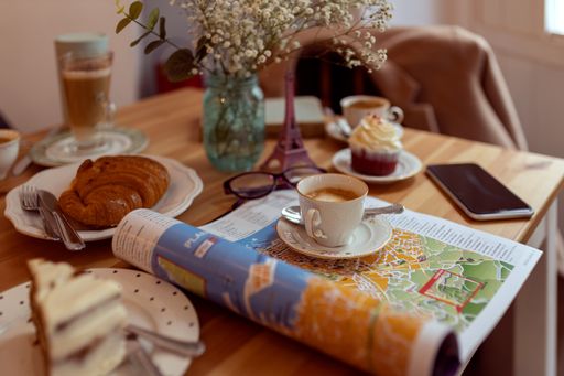 Different desserts and cups of coffee on a wooden table with a newspaper and a book