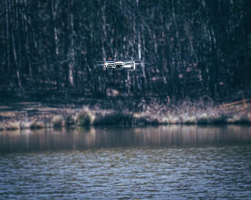A shallow focus of a drone flying over a lake with forest in background