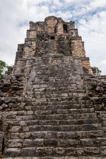 An image of the ancient Mayan ruins taken from a low angle, set against a cloudy sky
