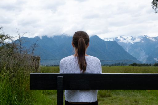 A lady in a ponytail sitting on a bench and admiring the view of the mountains covered in snow