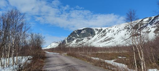 A panoramic shot of an empty countryside road amid snow-covered hills and areas under the blue sky