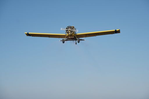 A single-engine propeller airplane flying in a perfectly clear blue sky