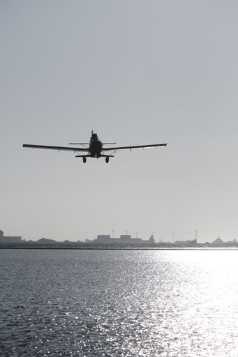 A vertical shot of a silhouette of a vintage single-engine aircraft with a propeller flying over  a lake