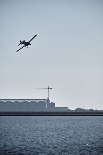 A vertical shot of a silhouette of a vintage single-engine aircraft with a propeller flying over  a lake