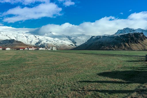 A sunny day in the green field surrounded by snowy mountains under the clear blue sky