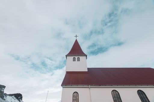 A low angle shot of a religious red-roofed building with a cross on top under a cloudy blue sky