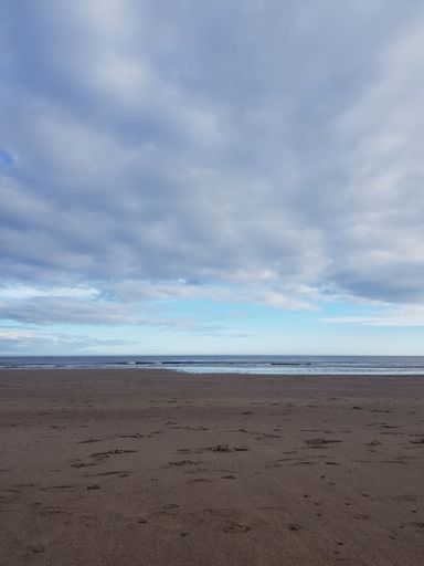 A vertical shot of soft ocean waves on a sandy beach under a cloudy sky