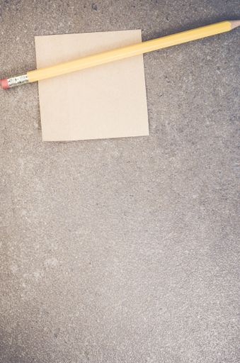 A top view closeup of a memo paper with a pencil on a toned rough stone textured surface