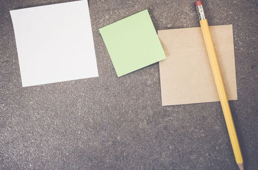 A top view closeup of memo papers with a pencil on a toned rough stone textured surface