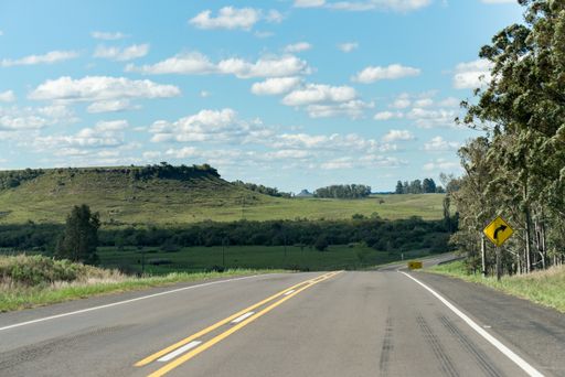 A lonely road and some hills on the background in Uruguay, next to Tacuarembo. The sky is full of small clouds and some trees on the right.