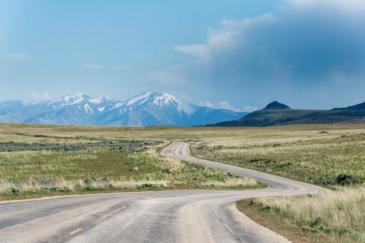 Winding road towards the snow capped mountains on the horizon with some prairies around it, at Antelope Island State Park, close to Salt Lake City, Ut