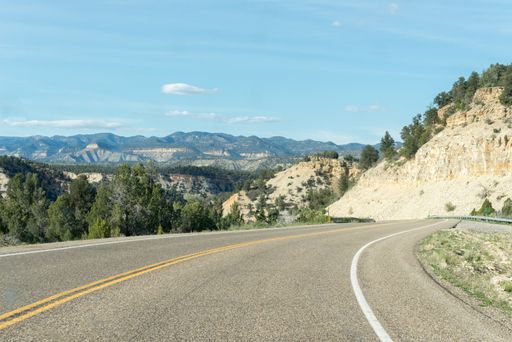 Lonely road between mountain ridges with some trees on each side of the road that turns to the right, somewhere in Utah, United States