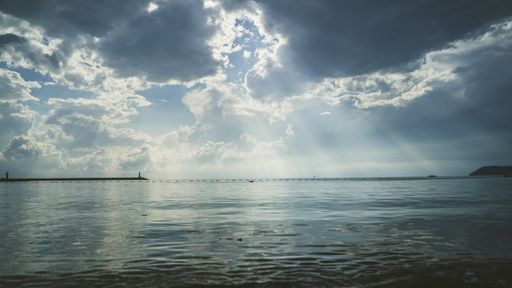 A majestic wavy sea under a dramatic heavy cloudscape with bright sun rays shining through clouds