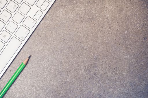 A top view closeup of the keyboard of a computer and a green pencil on a stone textured surface