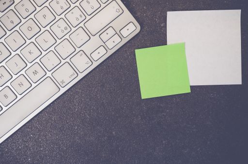 A top view of a computer keyboard and blank paper memos on a stone textured surface with copy space