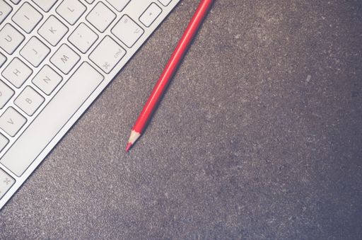 A top view of a computer keyboard and colored pencil on a stone textured surface with copy space