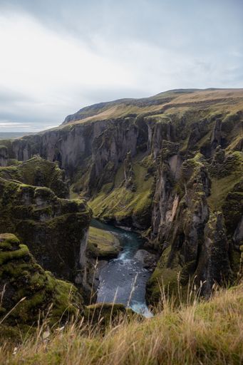A river surrounded by rocks covered in greenery and dry grass under a cloudy sky