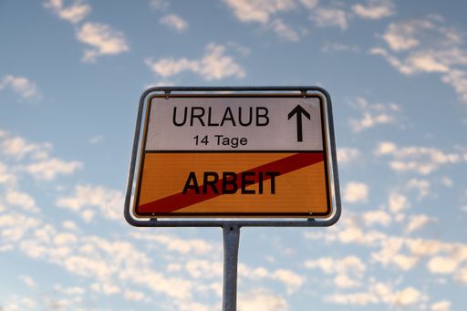 A directional road sign with the writings
translation: Vacation in 14 days, no work