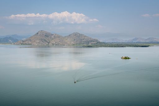 A high angle shot of a boat sailing on the Lake Skadar with mountains in the distance in Montenegro
