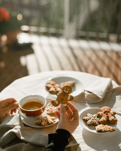 A vertical shot of female hands holding a christmas gingerbread man and a cup of coffee