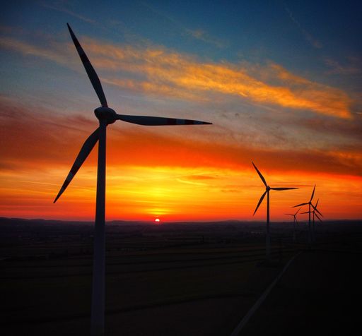 A breathtaking view of wind turbines spinning in the field on dark orange cloudy sunset sky background