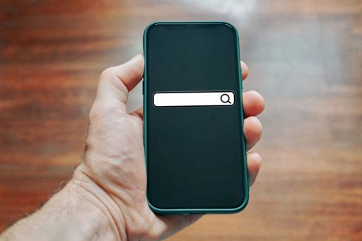 A man's hand holding a smartphone with a search field on the screen