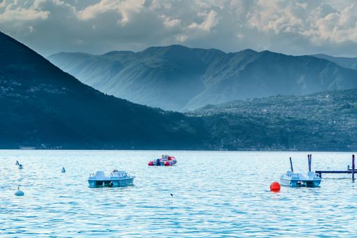 Three small sailboats moored in a serene Iseo lake in Italy, with mountains in the background