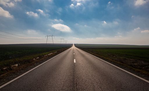 A country landscape with a straight road in a field under a cloudy sky