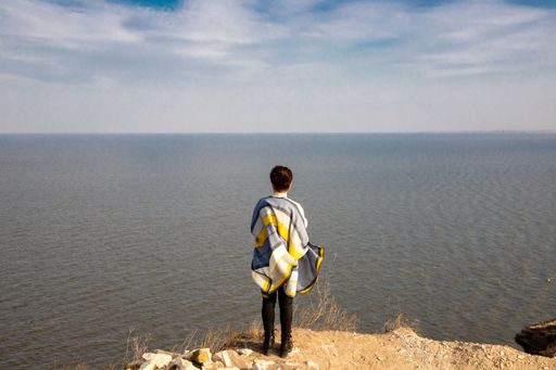 A women stands on a rocky cliff overlooking a blue body of water