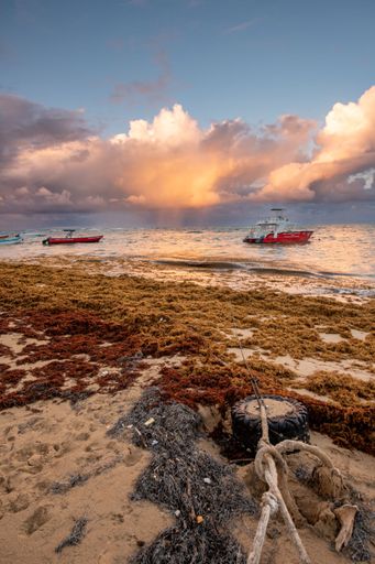 A scenic view of two boats docked on the shore of a beach, illuminated by the warm colors of the setting sun