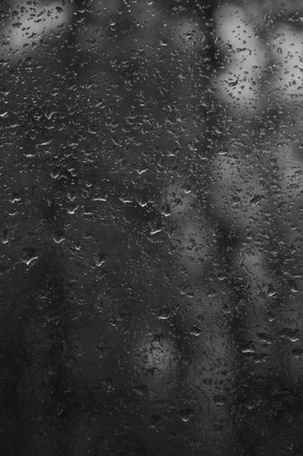 A grayscale shot of rain drops on the window with dark, blurry background