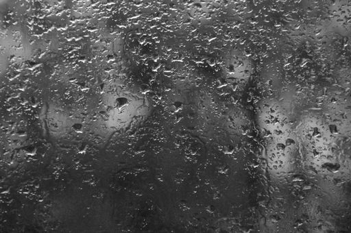 A grayscale shot of rain drops on the window with dark, blurry background