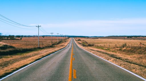 A wide shot of a lonely road in the middle of a dry desert continuing into the horizon under a clear blue sky