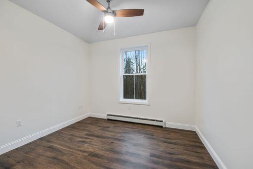 The interior of a room with a parquet floor, white walls, a ceiling fan and baseboard heater under the window