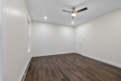 The interior of a room with a parquet floor, baseboard heater on the white wall, a ceiling fan and a door