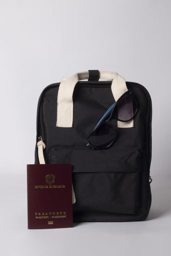 A vertical shot of black backpack with sunglasses, and passport on white background - travel concept
