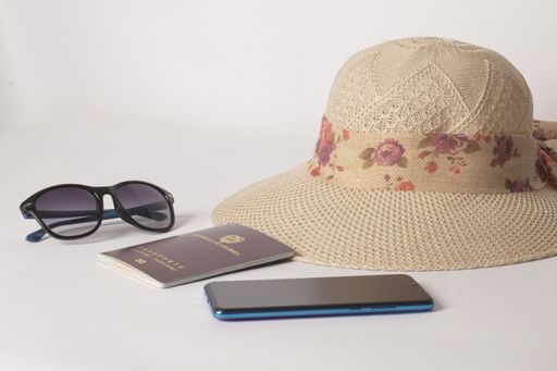 A view of sunglasses, passport, cellphone, and hat isolated on white background - travel concept