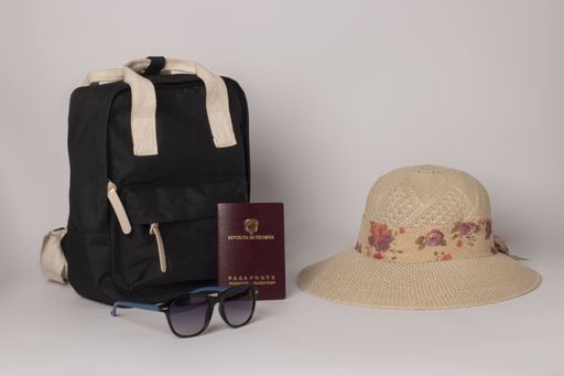 A black travel backpack with sunglasses, passport, and hat isolated on white background
