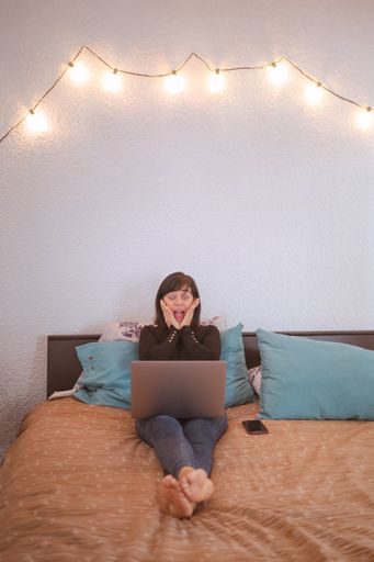 A vertical shot of a Caucasian woman looking at her laptop with a surprised face