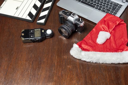 A top view of the laptop, camera, flash, film clapboard, and Santa hat on a wooden table