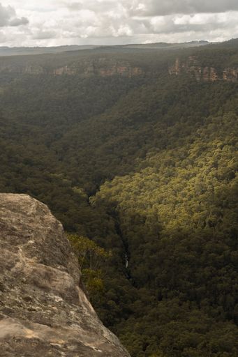 A high angle view of rocks and mountains covered in forests under a cloudy sky and sunlight