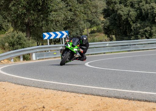 A male in a black outfit and blue helmet riding on a motorcycle in a  quiet street